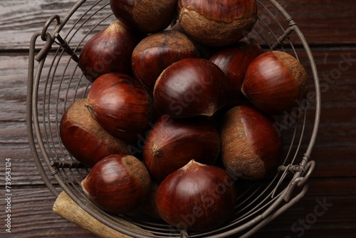 Sweet fresh edible chestnuts in metal basket on wooden table, top view