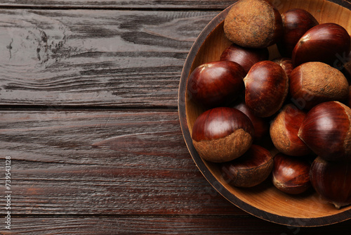 Sweet fresh edible chestnuts in bowl on wooden table, top view. Space for text