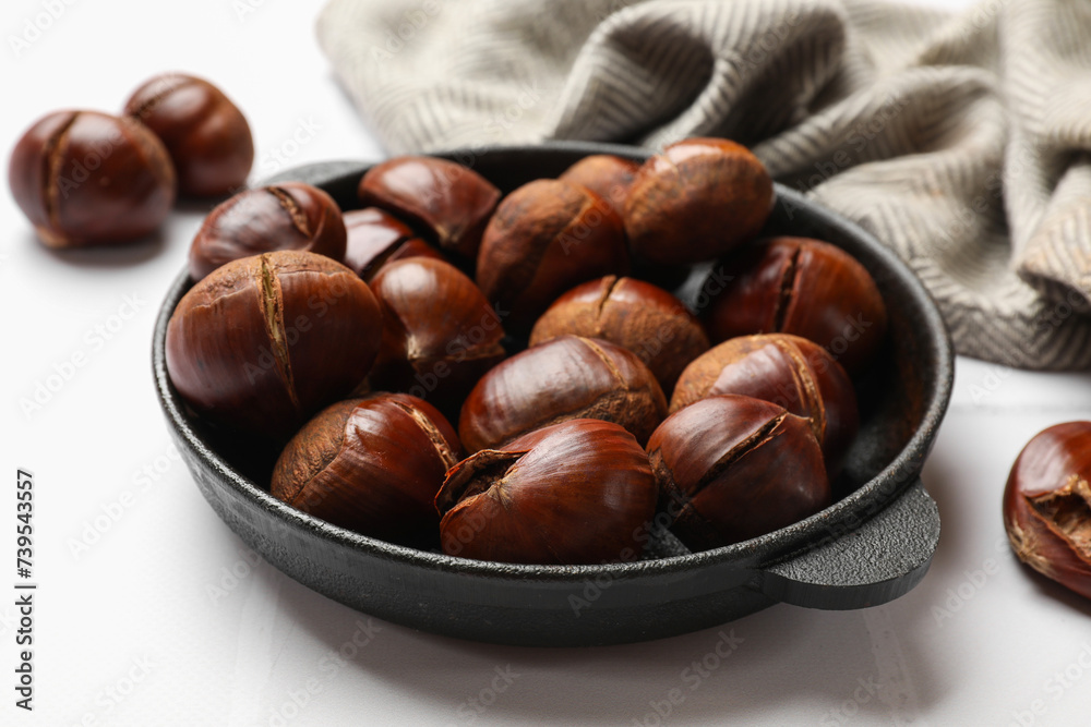 Fresh edible sweet chestnuts in frying pan on white tiled table, closeup Fresh edible sweet chestnuts in frying pan on white tiled table, closeup