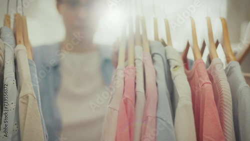 Fashionable. A young woman of European appearance dressed in modern clothes leisurely evaluates clothes on hangers in an elegant boutique. Current girl choosing color style of clothing for the evening photo