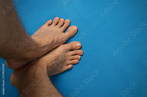 Pies de hombre joven latino, descalzo, apoyados sobre una esterilla azul. Dedo en martillo, juanetes y várices. Salud, podología, tratamiento y prevención de los trastornos del pie. Vista superior. photo