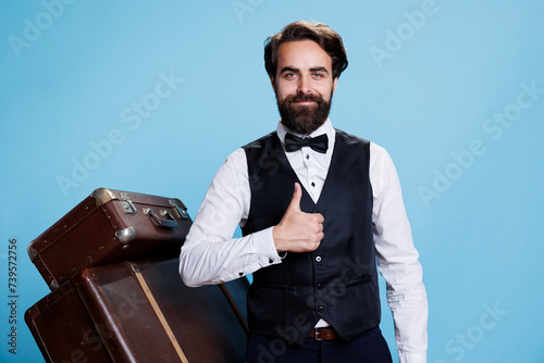 Bellboy gives the thumbs up whilst in studio, looking assured and enthusiastic on camera. Young hotel staff showing gesture of acceptance or consent while donning appropriate attire. photo