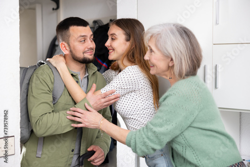 Young adult wife and her elderly mother meeting and embracing husband returning home