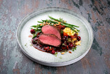 Traditionally roasted saddle of venison fillet with spaetzle, beans and pine nuts in game sauce served as close-up on a Nordic Design plate