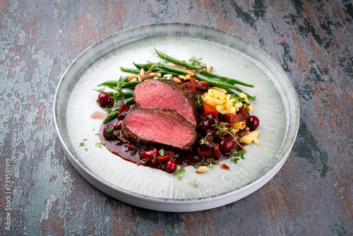 Traditionally roasted saddle of venison fillet with spaetzle, beans and pine nuts in game sauce served as close-up on a Nordic Design plate