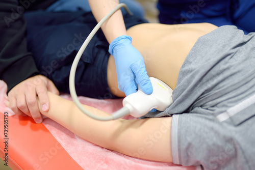 Doctor making abdominal ultrasound for boy using scanner machine. Female doc runs ultrasound sensor over patient tummy. Mother supports son during diagnosis examination of internal organs