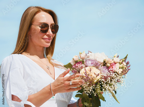 Obraz na płótnie Joyful Young Woman Holding a Bouquet of Flowers on a Beach with Blue Sky Background w salonie