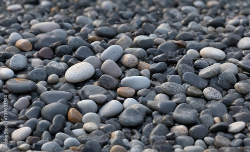Seamless dark black pile of small stone pebbles background texture. Beautiful shiny zen gravel river rocks widescreen wallpaper repeat pattern. High resolution nature closeup abstract
