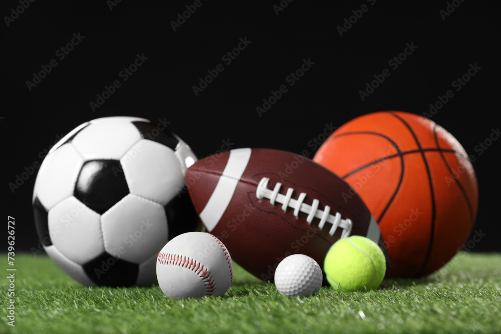 Many different sports balls on green grass against black background