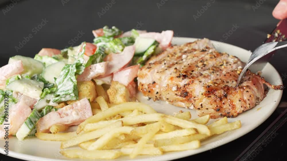 Hands slicing pork grilled stake served with french fries and vegetable salad on white plate Hands slicing pork grilled stake served with french fries and vegetable salad on white plate