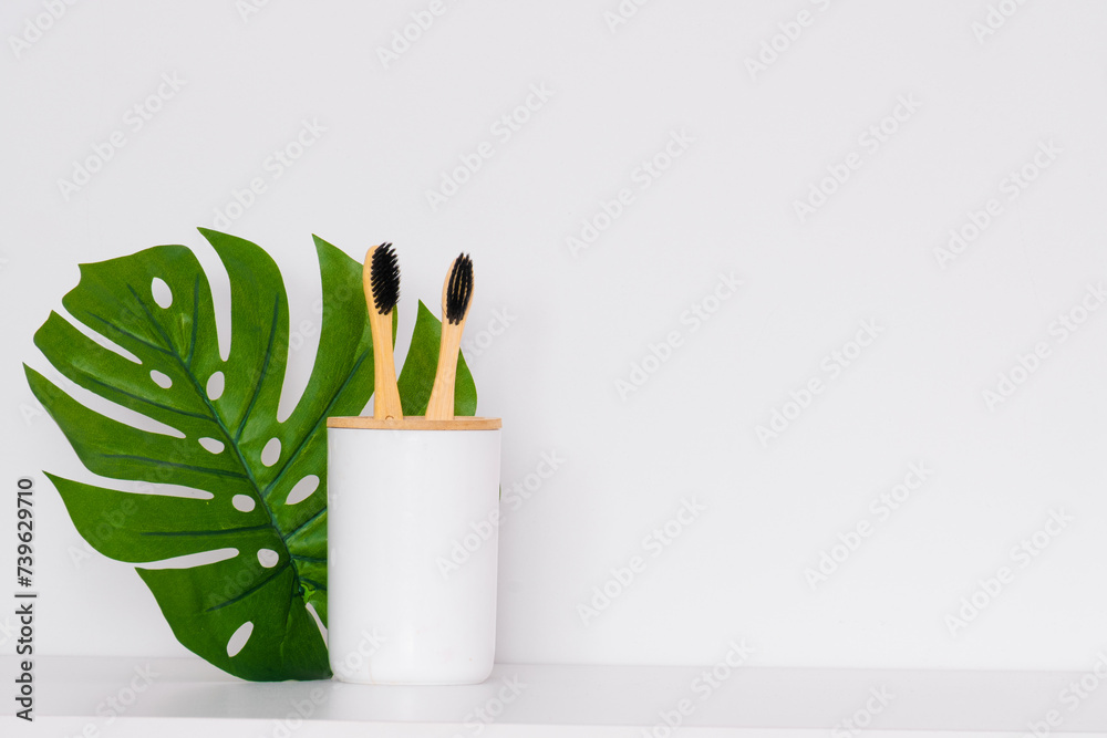 A glass with wooden toothbrushes and a plant on a white background. Minimalism A glass with wooden toothbrushes and a plant on a white background. Minimalism
