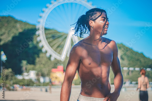 17-year-old afro-descendant teenager with braids in hair and no shirt, various facial expressions, lifestyle concept, ferris wheel of Camboriu resort in the background photo