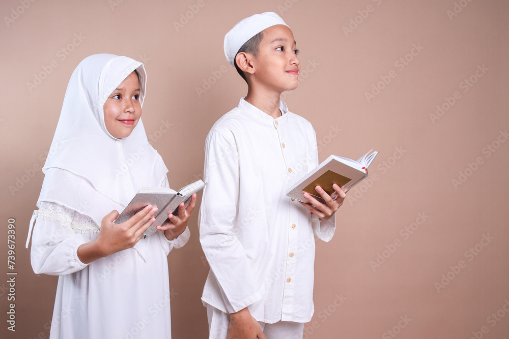 Two Asian muslim brother and sister sibling holding Quran and looking up to empty space Two Asian muslim brother and sister sibling holding Quran and looking up to empty space