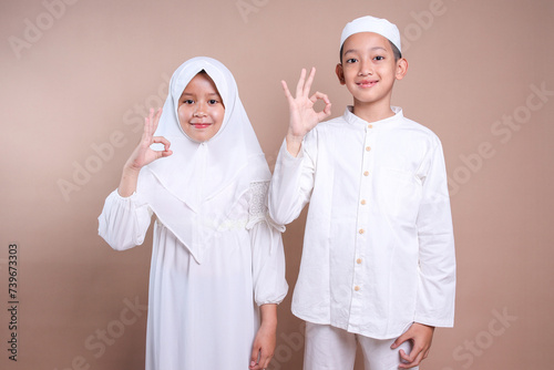 Asian muslim little boy and girl wear hijab and cap showing ok sign gesture with finger
