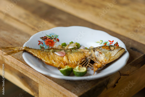 Ikan Peda  or ikan asin fried with sliced chili peppers, onions, and lime, served on a white plate. photo