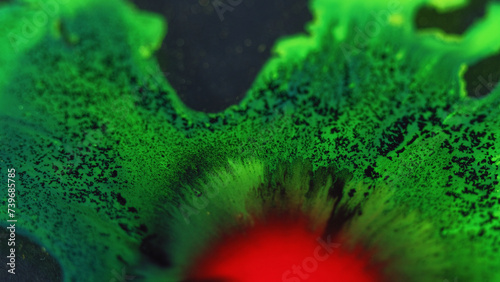 Paint drop. Ink spill. Defocused red green black color glowing fluid splash spreading flow motion particles texture dark abstract background.