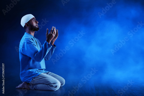 Young asian muslim man with beard praying on dark blue background
