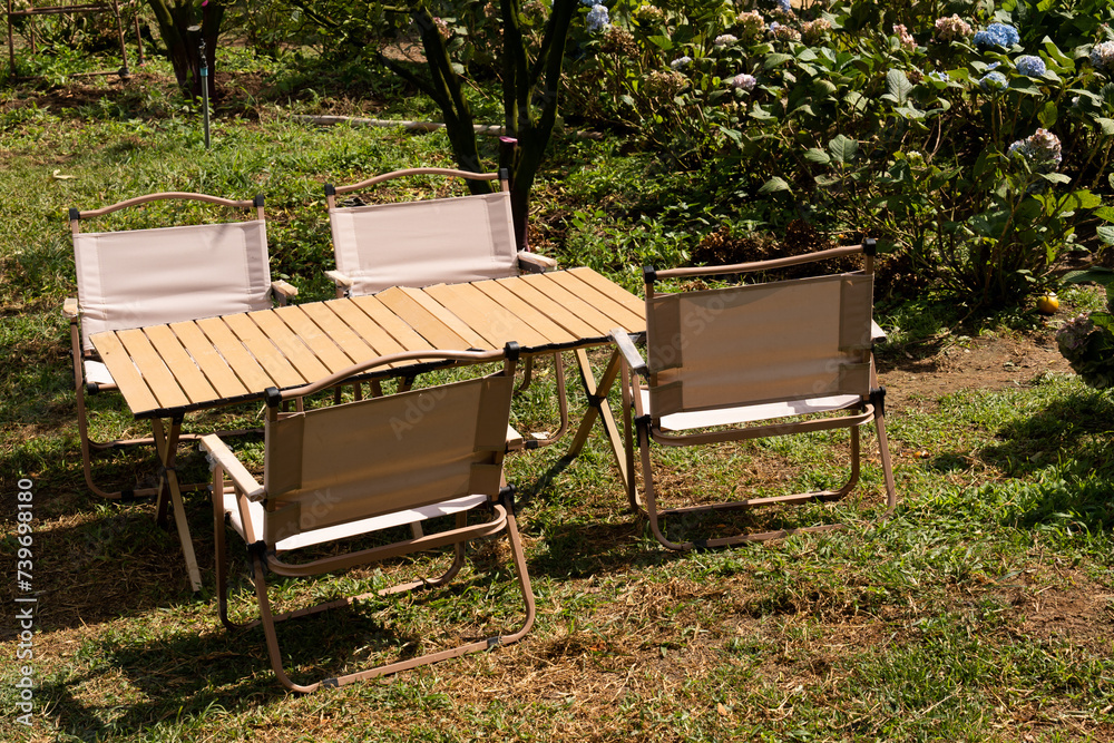 Inviting garden chairs and a wooden table await in a sunlight garden for camping or alfresco dining picnic offering a peaceful and relaxation amidst lush greenery Inviting garden chairs and a wooden table await in a sunlight garden for camping or alfresco dining picnic offering a peaceful and relaxation amidst lush greenery