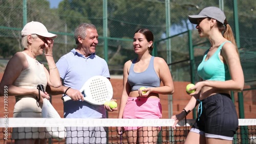 A group of positive Padel tennis players standing next to the net and talking merrily in open-air tennis court  photo