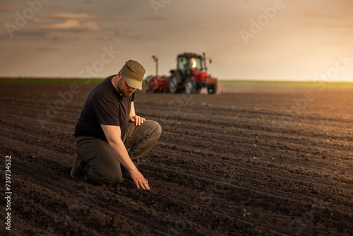 Farmer examing dirt while tractor is sowing field