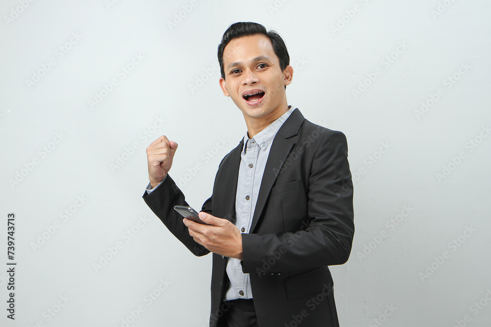 happy asian indonesian business man in suit holding smart phone on isolated background happy asian indonesian business man in suit holding smart phone on isolated background