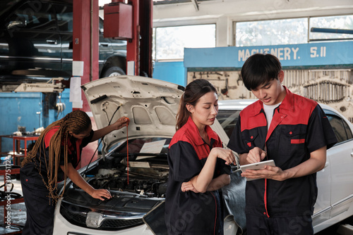 Two Asian professional mechanics  male supervisor engineer  and partner discuss and inspect repair work checklists at garage  service car maintenance  and fixing specialist occupations auto industry.