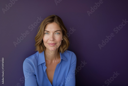 Pretty woman in blue blouse with short blonde hair looking at camera against a purple background