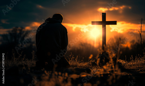A man in a field prays to God in front of a cross against the backdrop of dawn.
