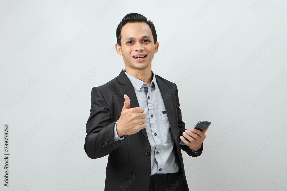 portrait of asian indonesian business man in suit holding smart phone with smlie and thumb up finger gesture on isolated background portrait of asian indonesian business man in suit holding smart phone with smlie and thumb up finger gesture on isolated background