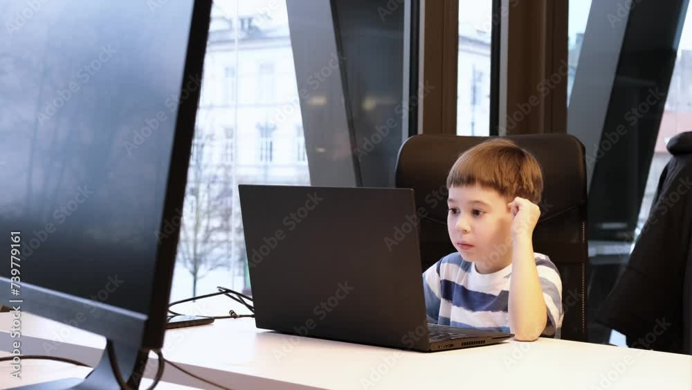 6 year boy using laptop in office. Distance self education. Programming lesson. Concentrated child solves difficult task. Use ChatGPT. Attentive kid looking at screen. Sedentary lifestyle concept. 4K 6 year boy using laptop in office. Distance self education. Programming lesson. Concentrated child solves difficult task. Use ChatGPT. Attentive kid looking at screen. Sedentary lifestyle concept. 4K