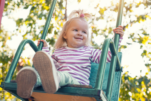 Happy little girl rides on a swing in a beautiful summer garden. Active summer holidays for children. © Dmytro Titov