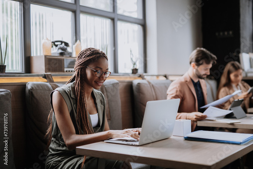 Beautiful businesswoman working on laptop in modern office. Group of freelancers working in shared work area. Concept of coworking, common workspaces for business, startups.