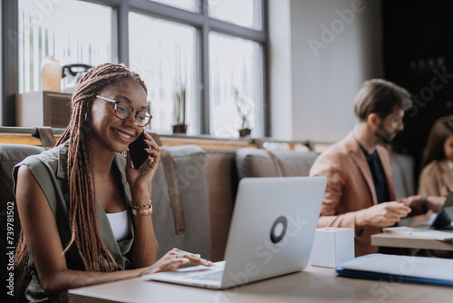 Beautiful businesswoman making phone call in modern office. Group of freelancers working in shared work area. Concept of coworking, common workspaces for business, startups.
