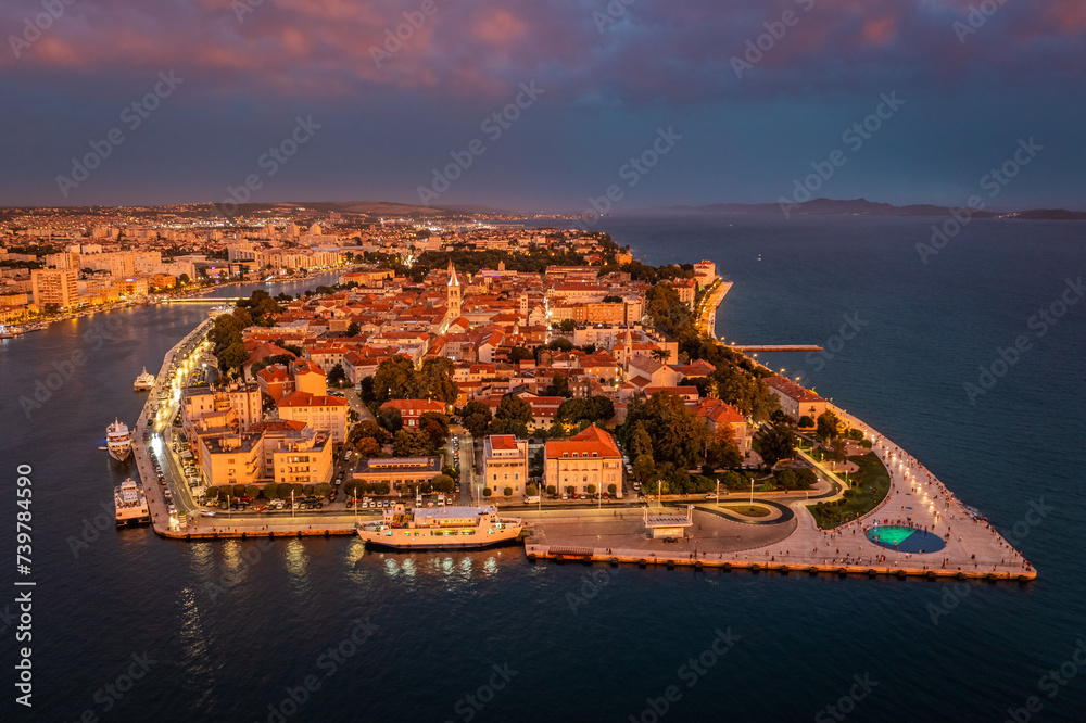 Zadar, Croatia - Aerial panoramic view of golden glowing old town of Zadar with the greeting to the sun monument, dramatic sunset lights and purple clouds on a beautiful summer afternoon in Dalmatia
