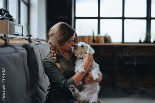 Portrait of beautiful young woman holding her dog in hands. Cute white dog in arms of loving owner. With dog in coffe shop.
