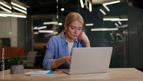 Young woman in casual outfit sitting at desktop and typing on laptop while getting annoyed with difficult task. Nervous female feeling bored while working on computer and sending emails to customers. photo