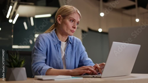 Attractive woman in casual clothes working at laptop and feeling tired with boring job while sitting at office. Unmotivated manager typing slowly on computer and waiting for the end of workday. photo