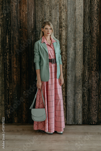 beautiful fashionable blonde girl stands in a pink dress and a mint jacket with a bag in her hands