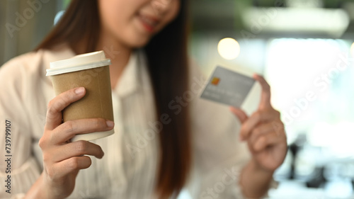 Select focus on woman hand holding paper cup of coffee and looking at credit card