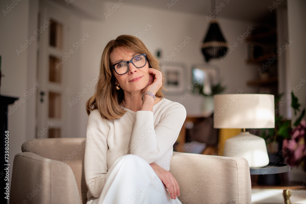 Attractive mid aged woman sitting in her modern home and relaxing in an armchair Attractive mid aged woman sitting in her modern home and relaxing in an armchair