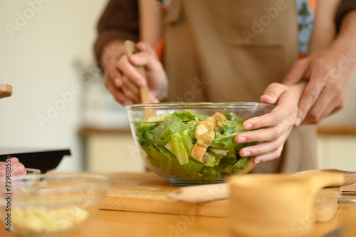 Loving young couple embracing and preparing healthy salad meal in kitchen at home