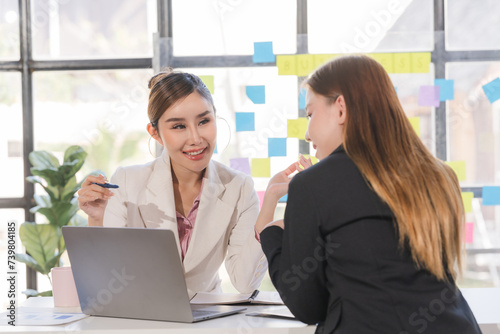 Two young Asian business woman talk, consult, discuss working with new startup project idea presentation analyze plan marketing and investment in the office.