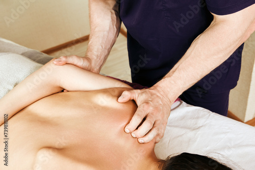Massage shoulder area of woman who is lying face down on a massage table.