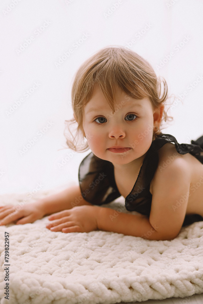 Studio portrait of beautiful baby girl in black uotfit lying on plush knitted blanket. Copy space for text Studio portrait of beautiful baby girl in black uotfit lying on plush knitted blanket. Copy space for text