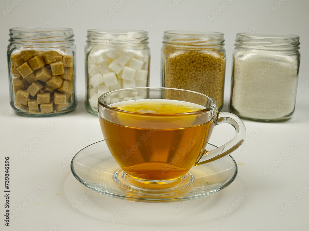 A glass cup of tea against the background of the glass jars with various types of sugar A glass cup of tea against the background of the glass jars with various types of sugar