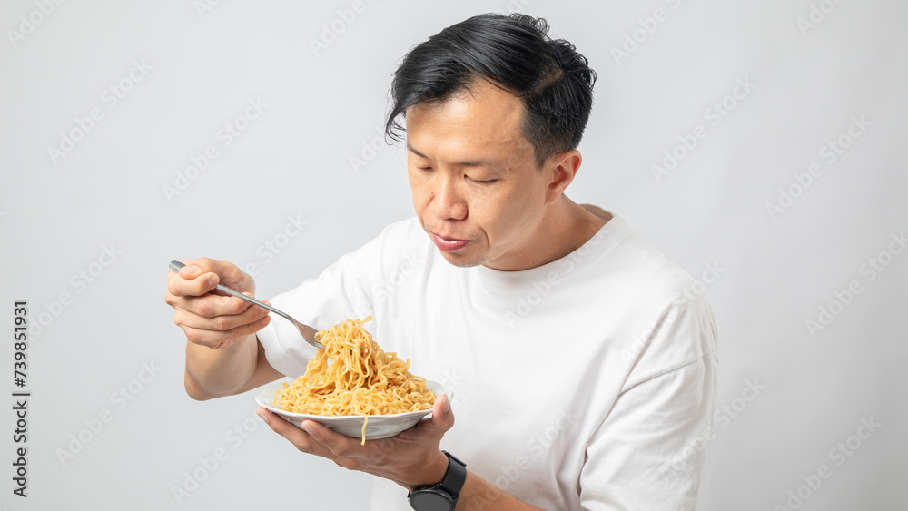 Portrait of an Indonesian Asian man, wearing a white T-shirt, enjoying eating noodles, isolated against a white background. Portrait of an Indonesian Asian man, wearing a white T-shirt, enjoying eating noodles, isolated against a white background.