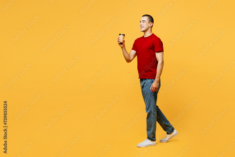 Full body young middle eastern man he wears red t-shirt casual clothes hold takeaway delivery craft paper brown cup coffee to go isolated on plain yellow orange background studio. Lifestyle concept. Full body young middle eastern man he wears red t-shirt casual clothes hold takeaway delivery craft paper brown cup coffee to go isolated on plain yellow orange background studio. Lifestyle concept.