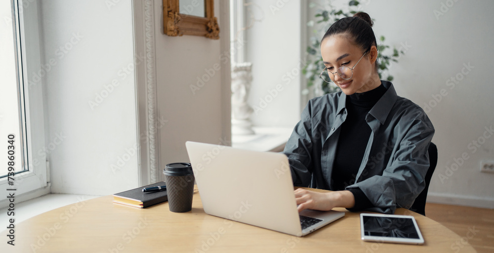 Focused woman working on laptop in a minimalist home office, symbolizing remote work and contemporary design. Focused woman working on laptop in a minimalist home office, symbolizing remote work and contemporary design.