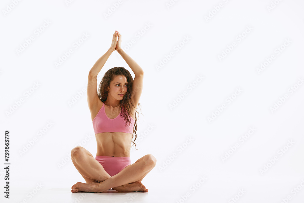Young beautiful, naked woman sitting in lotus pose raised arms doing yoga exercises against white studio background. Concept of self care, healthy lifestyle, fitness, mindfulness, female health.