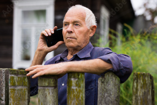 Senior man leaning on fence and talking on phone photo